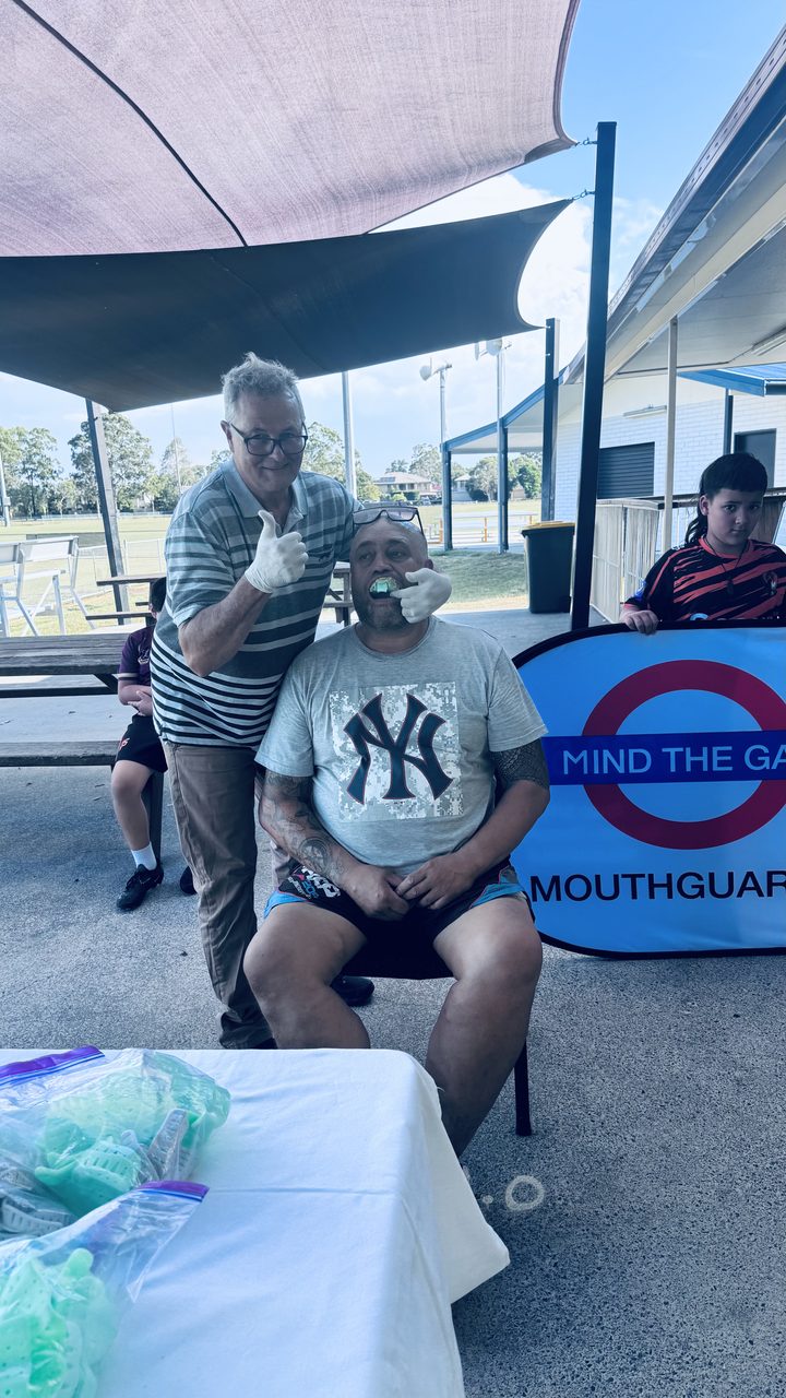 A Mind The Gap prosthetist fitting a mouthguard impression at a Gold Coast club day, beside the branded banner