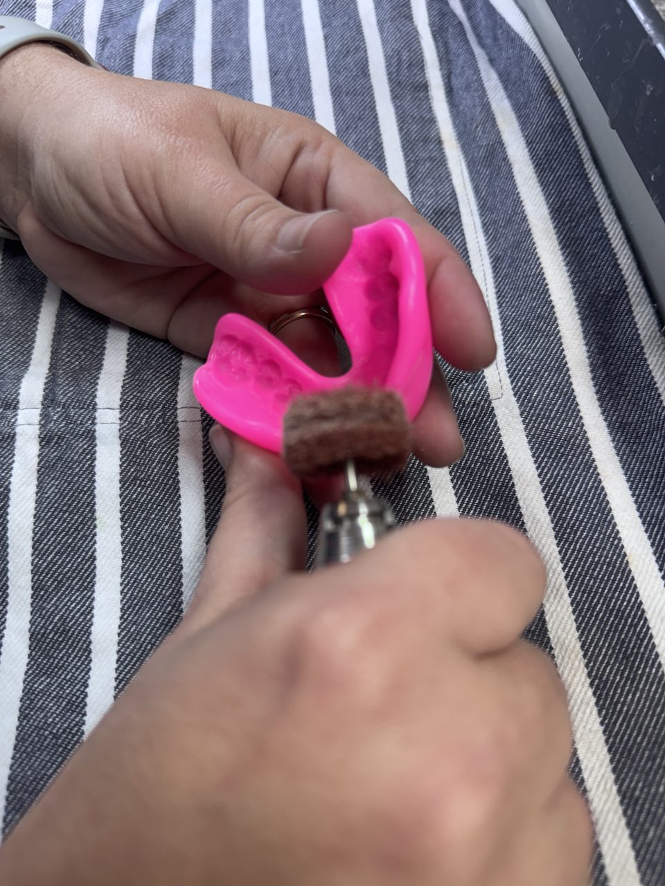 A pink mouthguard being polished by hand at the Helensvale bench