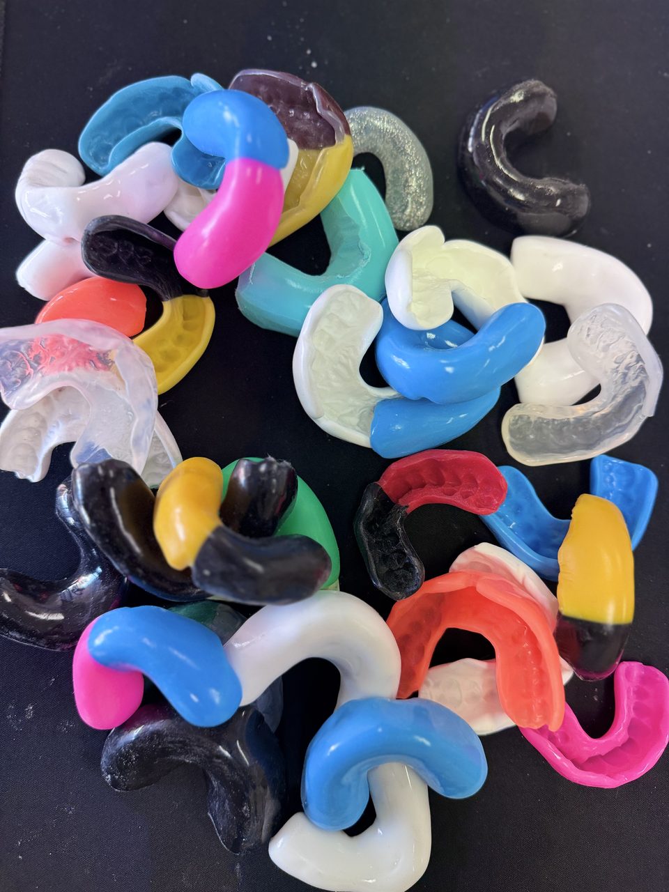 Two dozen finished custom mouthguards in club colours, laid out on a black bench